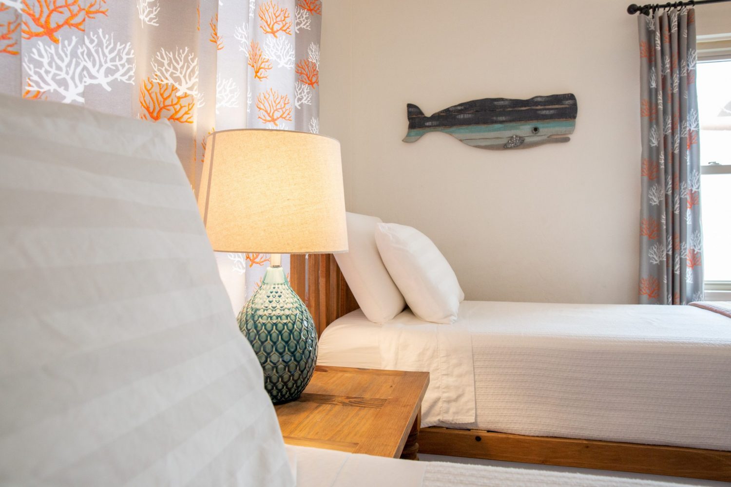 two beds with a ceramic fish on the wall and a lamp in between